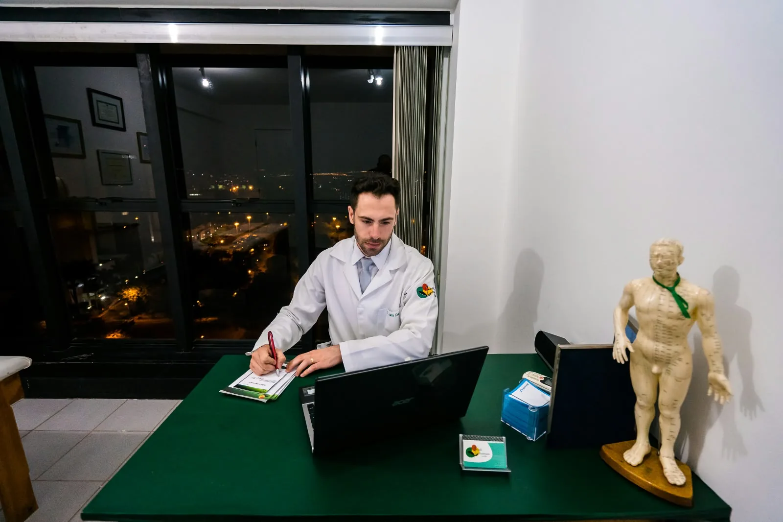 Lucas Ceratti escrevendo no consultório, com a vista de Brasília pela janela