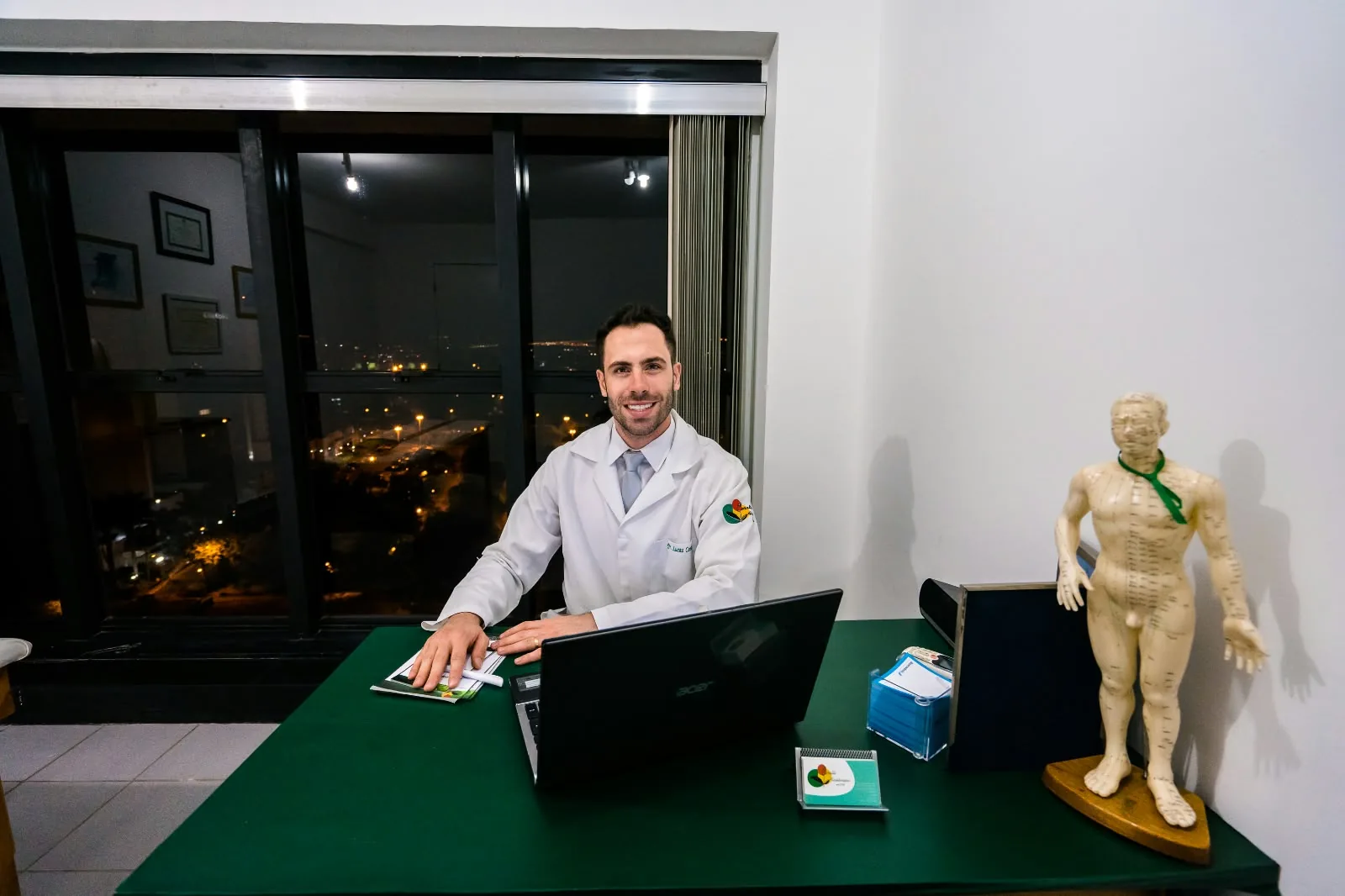 Lucas Ceratti no consultório à noite, com a vista de Brasília pela janela